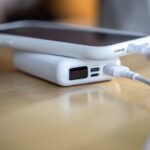 Portable power bank charging an iPhone via cable on a wooden desk with compact fast-charging battery pack