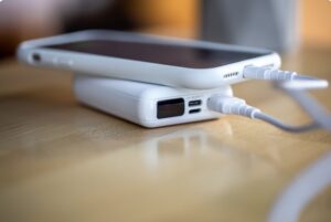 Portable power bank charging an iPhone via cable on a wooden desk with compact fast-charging battery pack