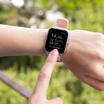 Person wearing a smartwatch and tapping its screen outdoors.