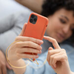 Two women relaxing together while using a smartphone with a slim orange phone case.