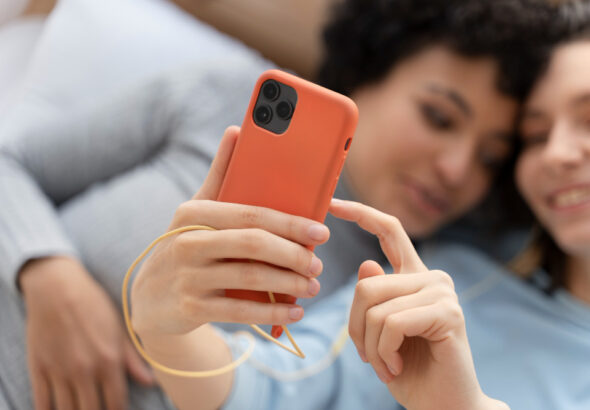 Two women relaxing together while using a smartphone with a slim orange phone case.