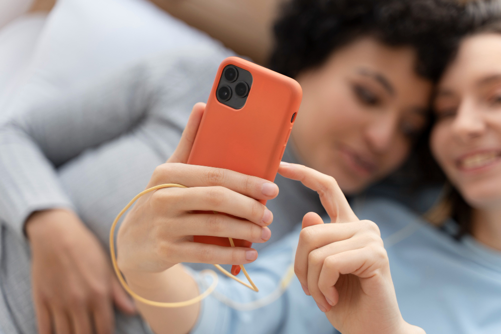 Two women relaxing together while using a smartphone with a slim orange phone case.